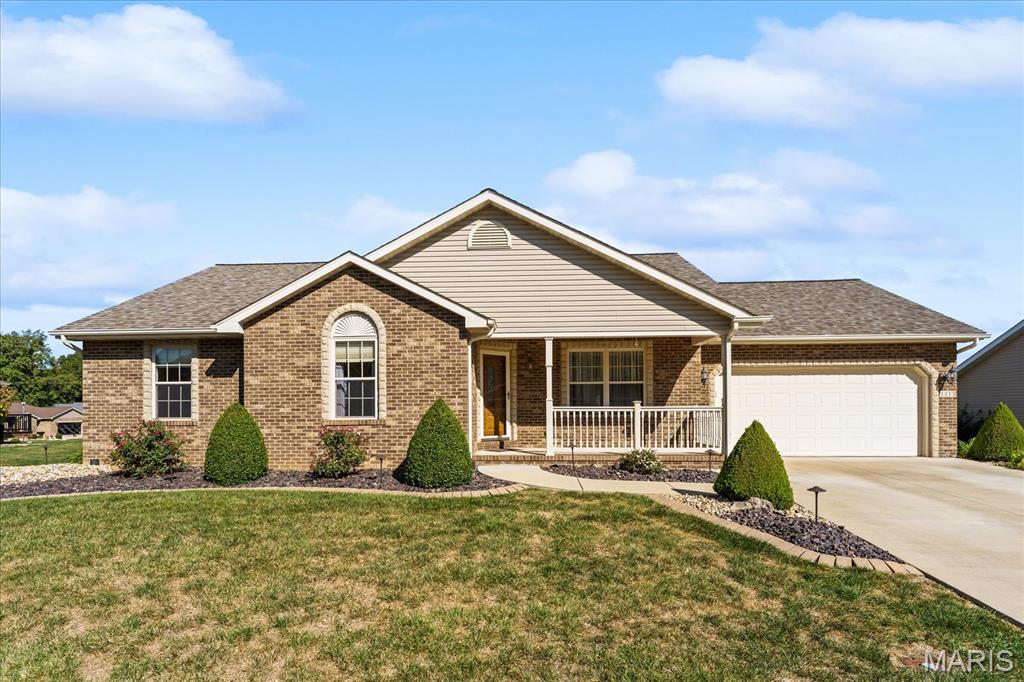 Brick ranch home with a covered porch, attached garage, and landscaped front lawn.