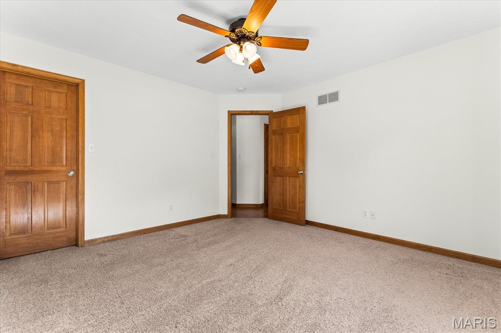 Vacant carpeted bedroom with a wood ceiling fan and two paneled doors.