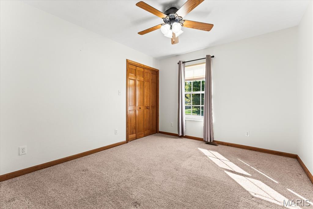 Empty bedroom with beige carpet, a wooden closet, and sunlight across the floor.