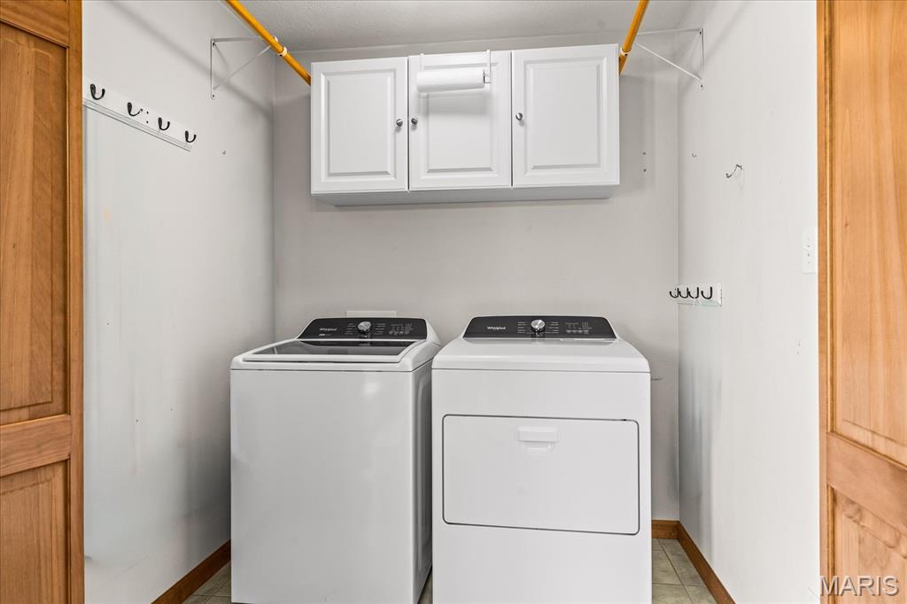Laundry room with side-by-side washer and dryer, overhead cabinets, hooks, and hanging rods.
