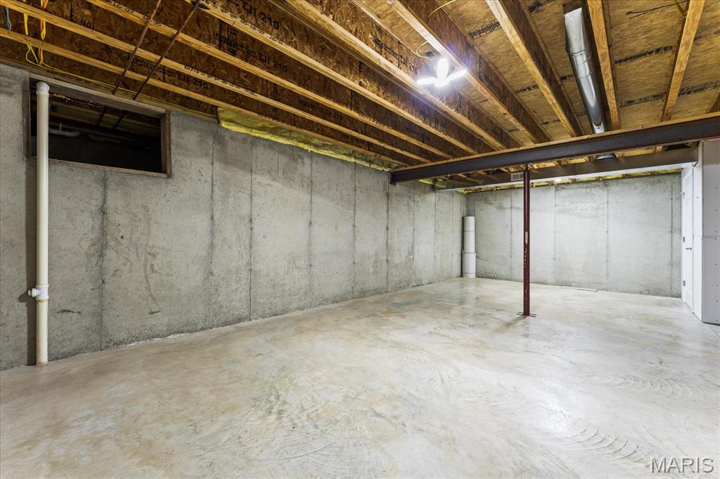Unfinished basement with concrete walls and floor, exposed ceiling joists, and a steel support post.