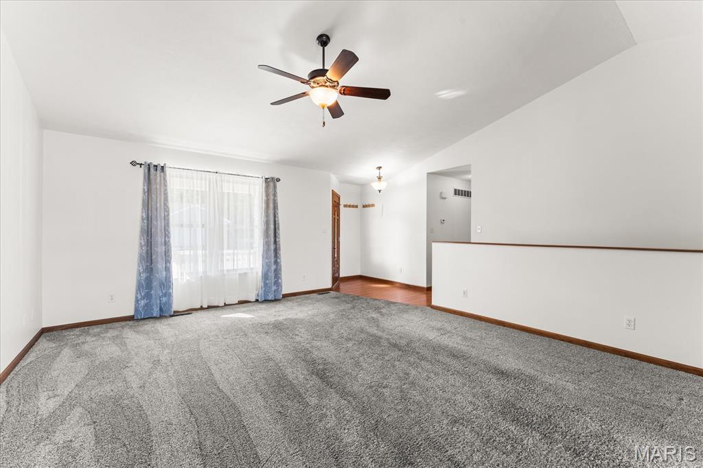 Vacant living room with gray carpet, a ceiling fan, and a large window with blue curtains.