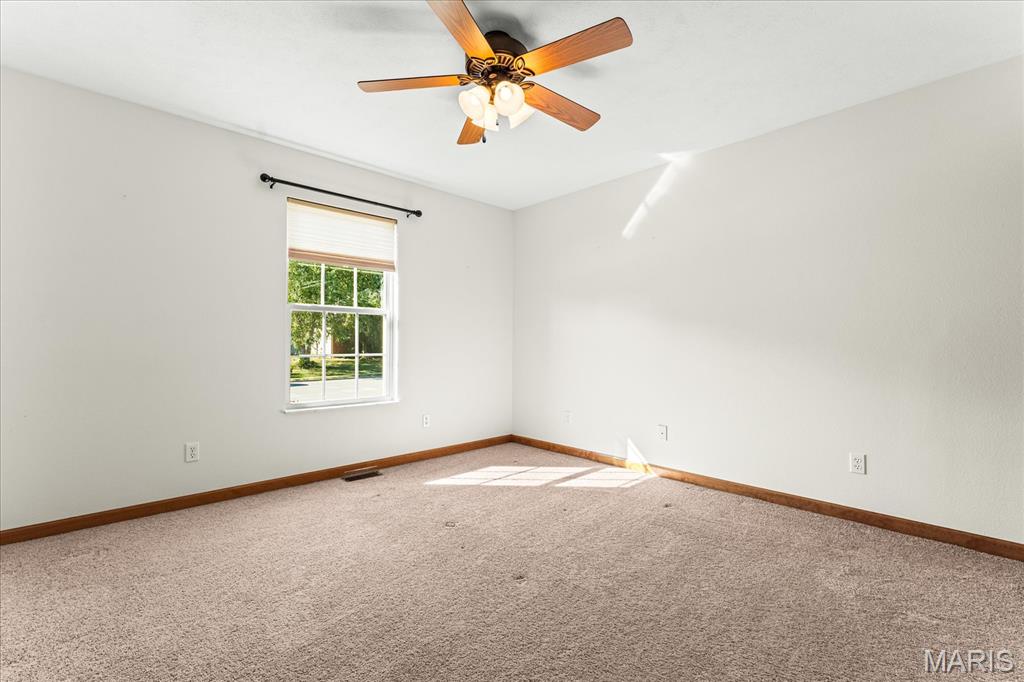 Empty bedroom with beige carpet, a window, and a wood ceiling fan with lights.