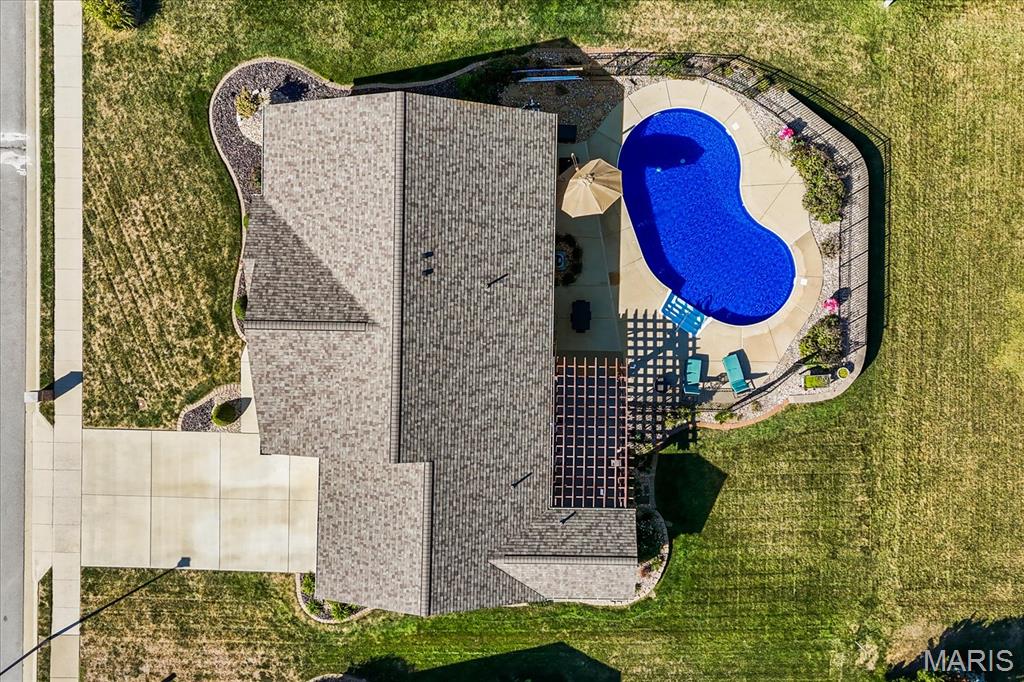 Aerial view of a house with a fenced backyard pool, patio, and broad lawn.