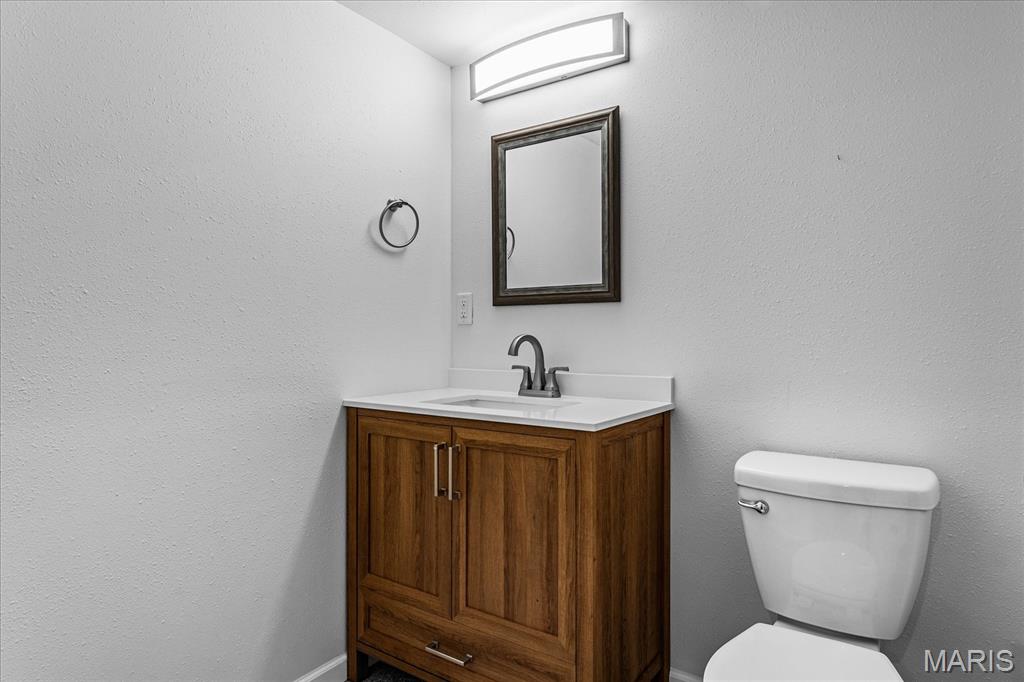Bathroom with a wood vanity, white sink, toilet, and framed mirror.