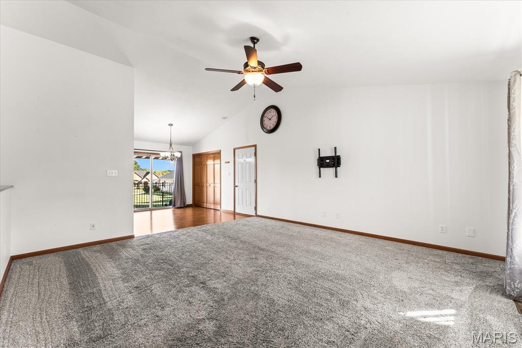 Empty living room with gray carpet, ceiling fan, and an opening to a dining area.