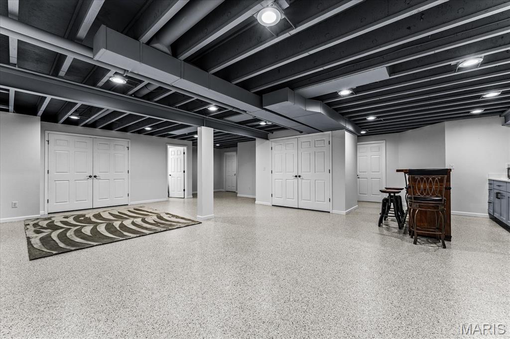 Finished basement recreation room with an exposed-beam ceiling, patterned rug, and small bar.