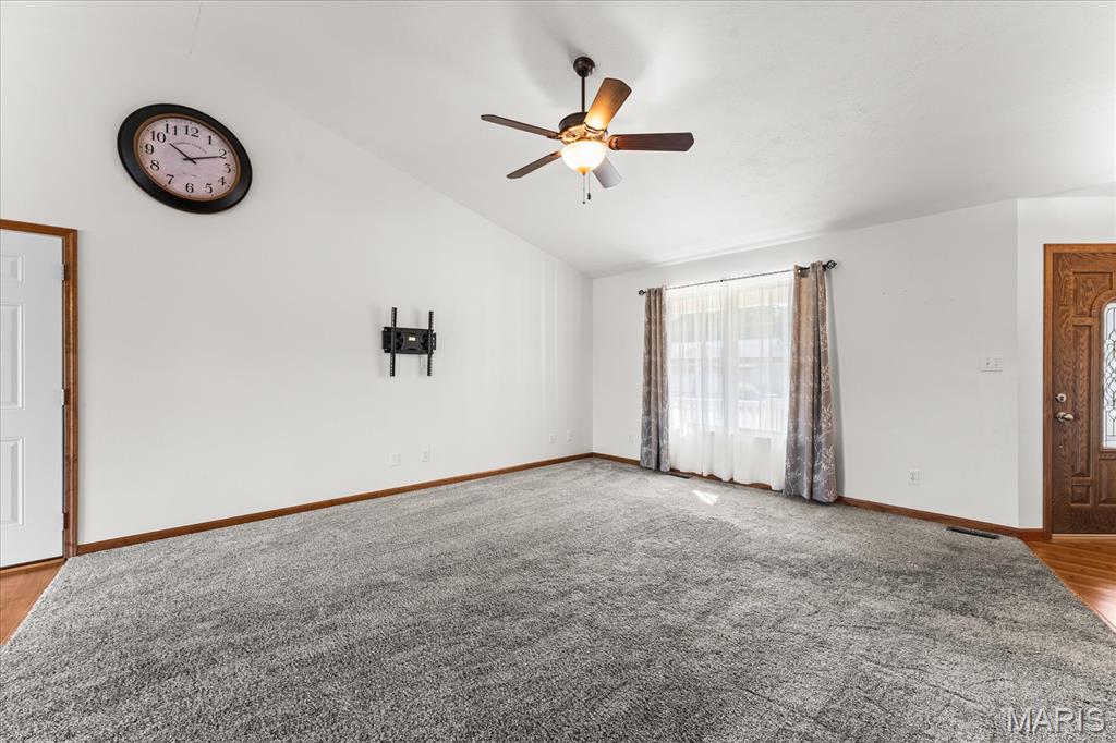 Empty living room with gray carpet, ceiling fan, curtained window, and wood-trimmed doors.