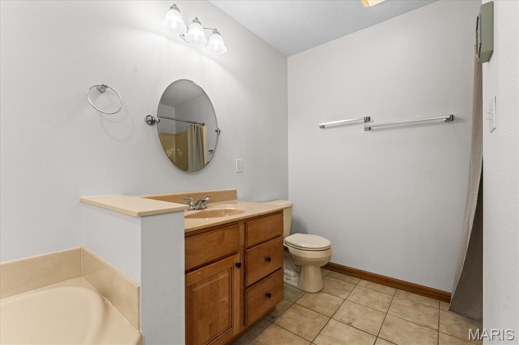Bathroom with a wood vanity, oval mirror, toilet, and partially visible bathtub.
