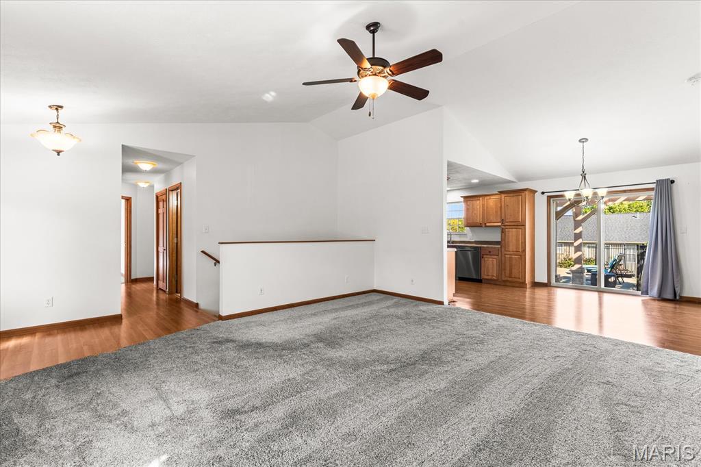 Open-plan living area with a large gray carpet and ceiling fan, adjoining the kitchen and sliding glass doors.