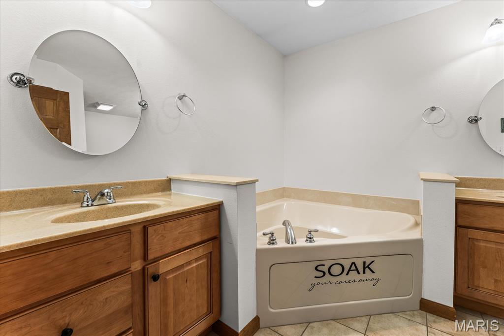 Bathroom with a corner soaking tub, wood vanities, tan counters, and round mirrors.