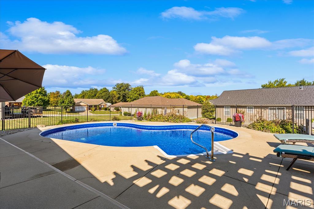 Outdoor swimming pool with a concrete deck, safety fence, and lounge chairs.