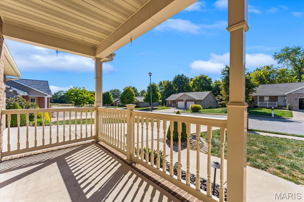 Covered front porch with tan columns and white railings overlooking a quiet residential street.
