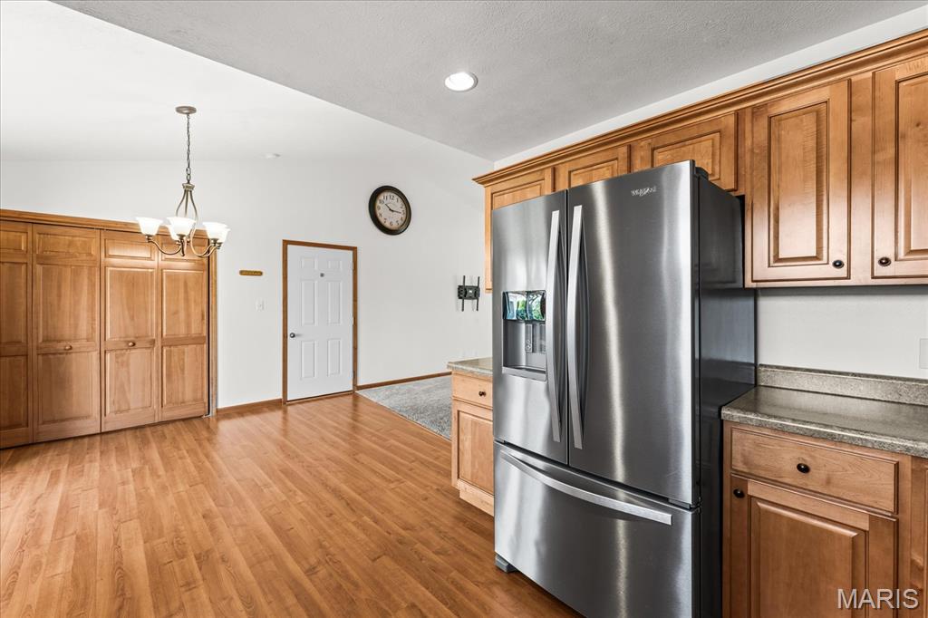 Kitchen with extensive wood cabinetry, a stainless-steel refrigerator, stone counters, and warm wood flooring.