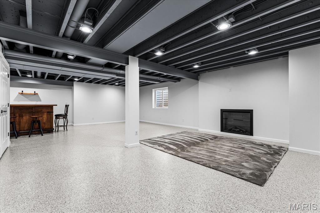 Finished basement recreation room with exposed ceiling beams, an electric fireplace, and a small bar.