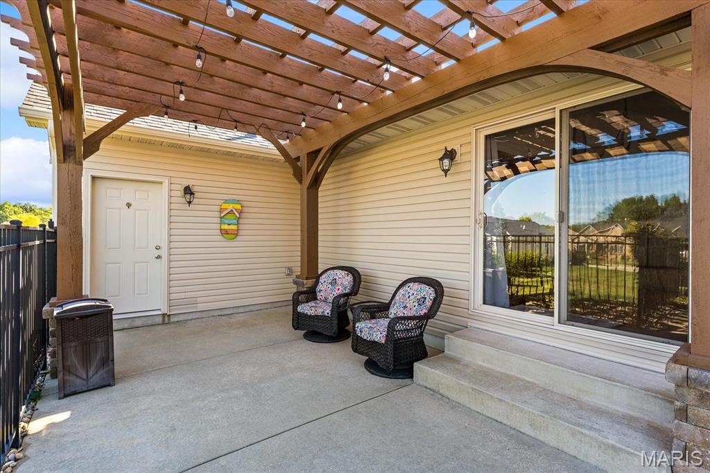 Covered patio with a wooden pergola, string lights, and two cushioned wicker chairs.