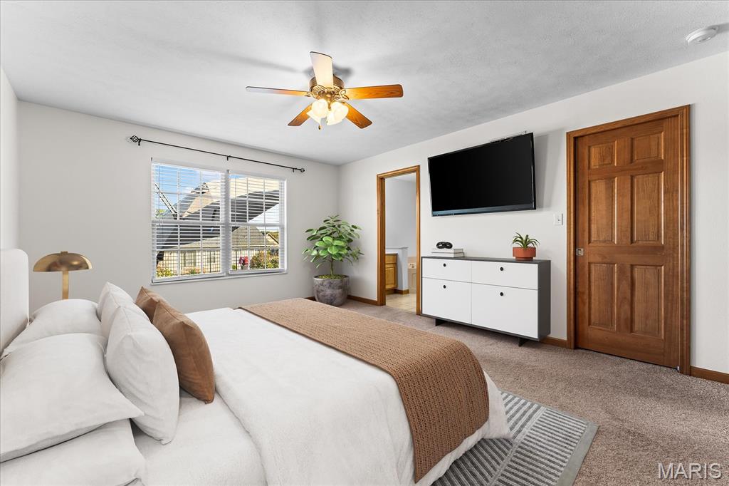 Furnished bedroom with a white bed, tan throw, ceiling fan, television, and wooden paneled door.