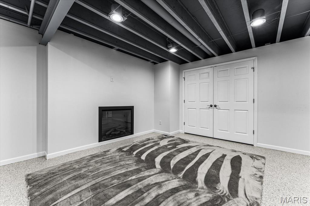 Finished basement room with a black fireplace, white double doors, exposed beams, and a patterned rug.