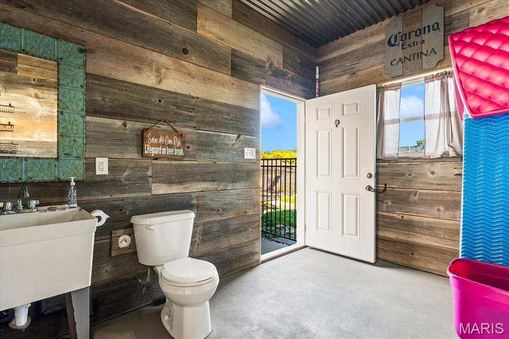 Rustic bathroom with weathered wood walls, a utility sink, toilet, and open door to an exterior landing.