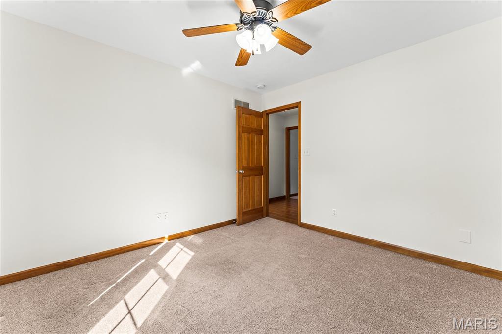 Empty bedroom with beige carpet, wood trim, and a ceiling fan with lights.