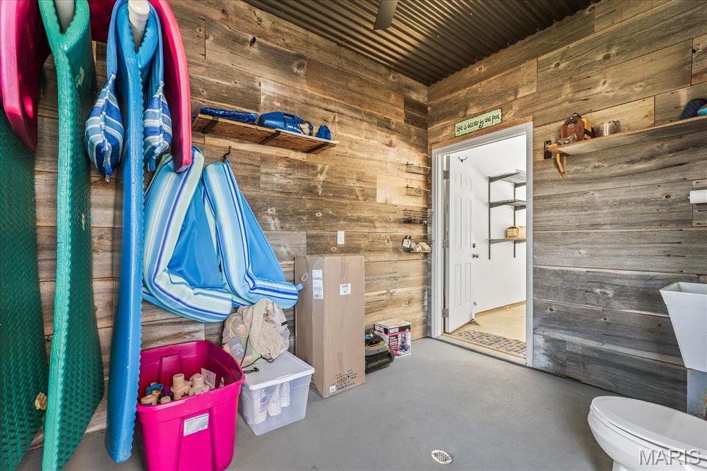 Poolside bathroom with wood-plank walls, a toilet, sink, and colorful floats stored along one wall.