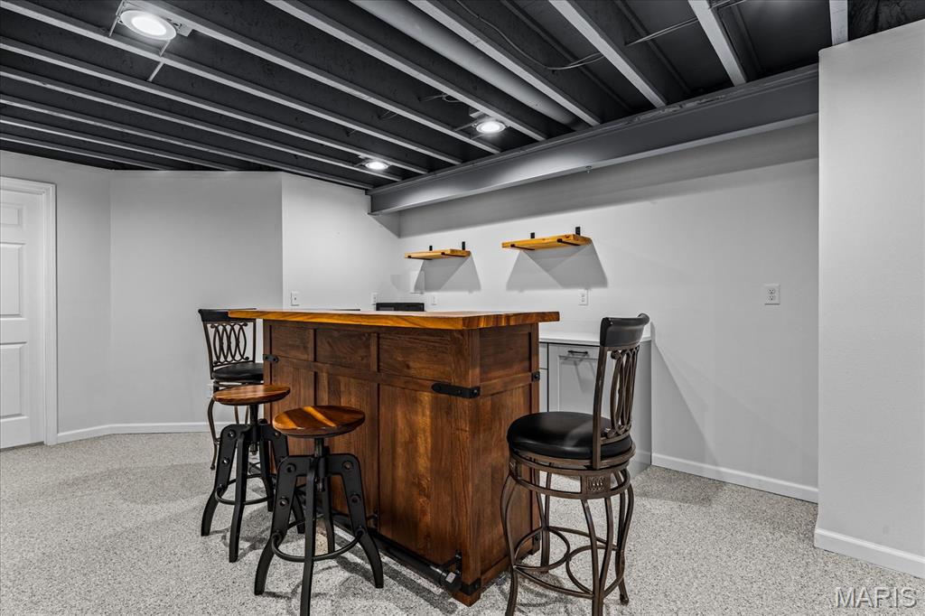 Finished basement recreation area with a wooden bar, stools, and exposed ceiling beams.