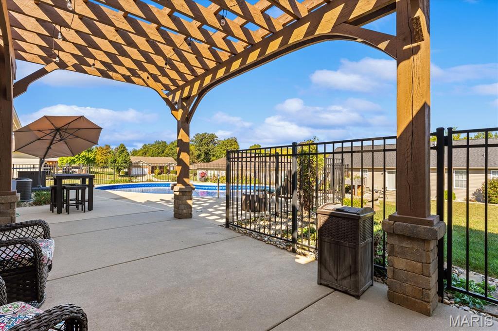 Patio beneath a wooden pergola overlooking a fenced swimming pool.