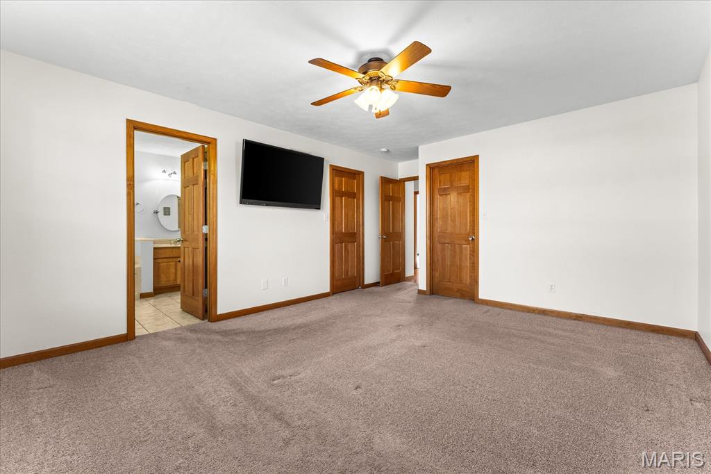Empty carpeted bedroom with a ceiling fan, wall-mounted television, and adjoining bathroom.