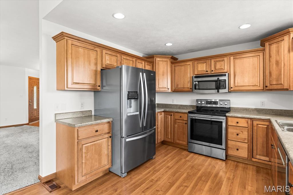 Kitchen with wood cabinetry, granite counters, stainless steel appliances, and wood flooring.