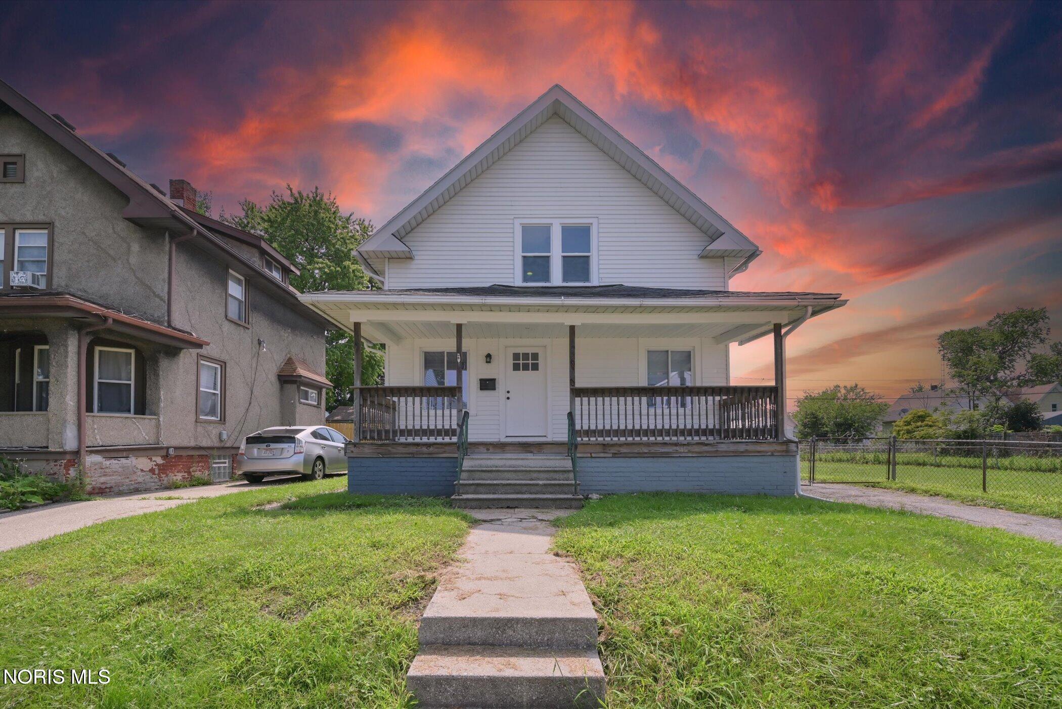 White two-story house with a wide covered porch and concrete front walk beneath a vivid dusk sky.