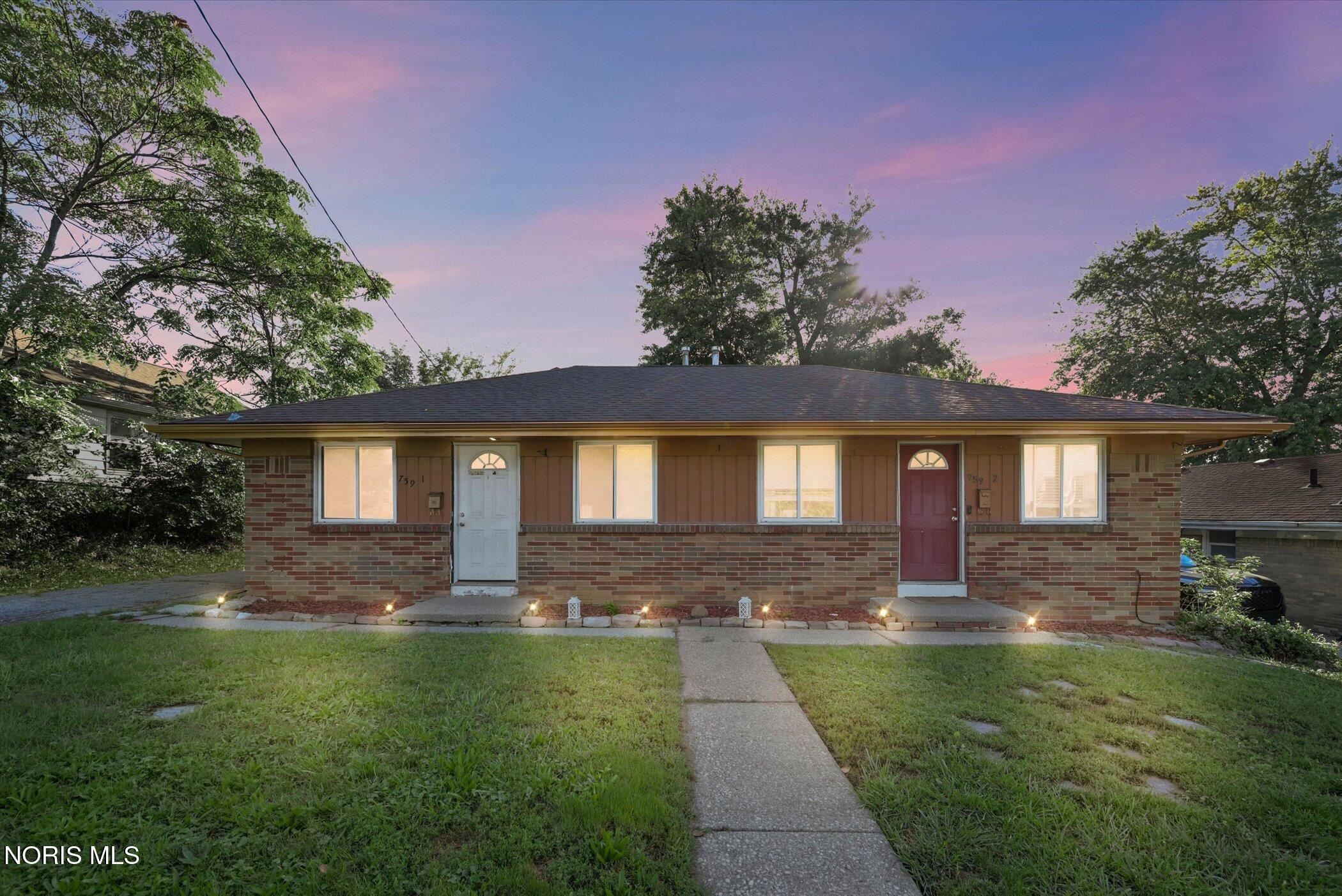 Single-story brick home with two front doors, illuminated windows, and a walkway through the lawn at dusk.