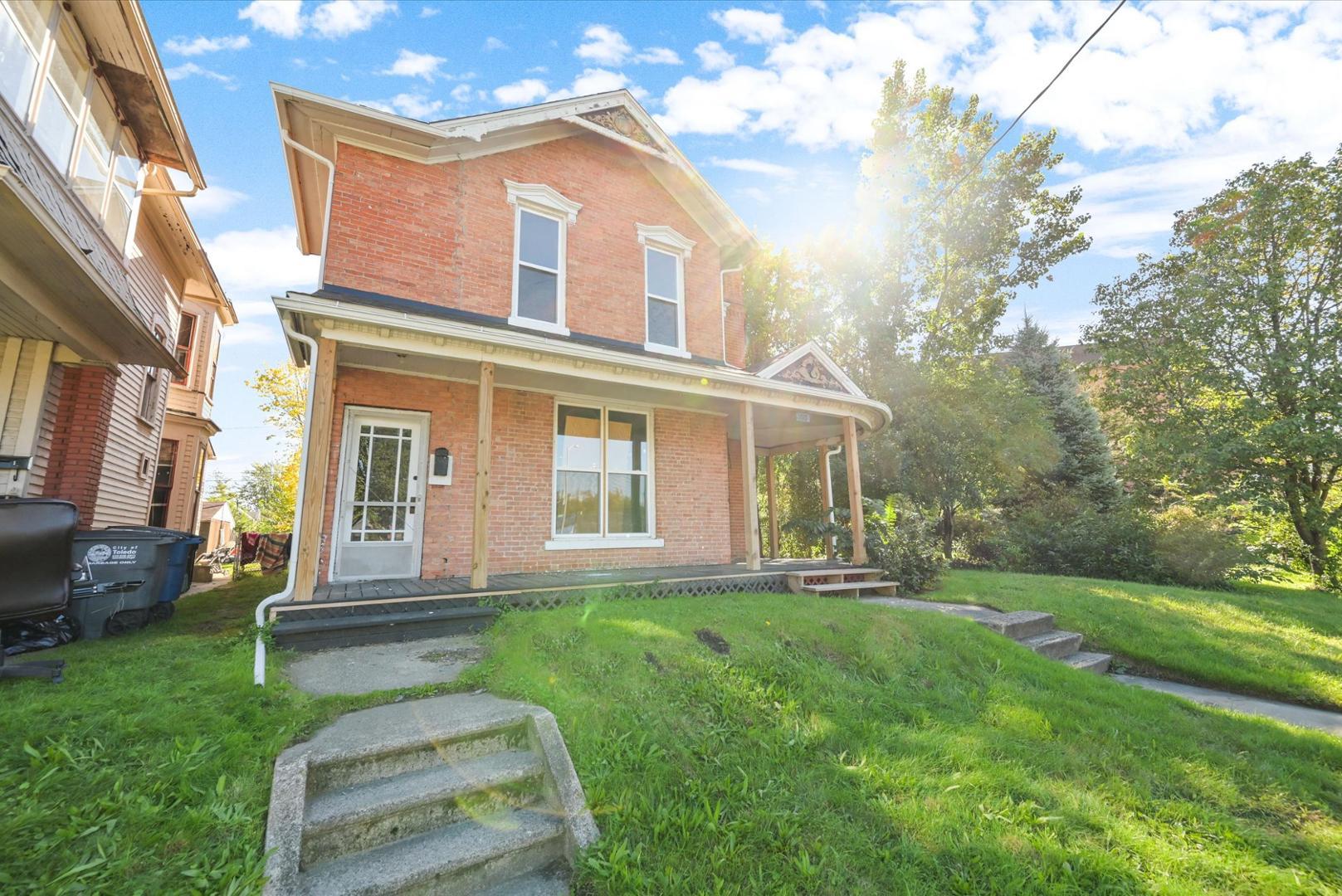Two-story brick house with a covered porch, white trim, and a grassy front yard.