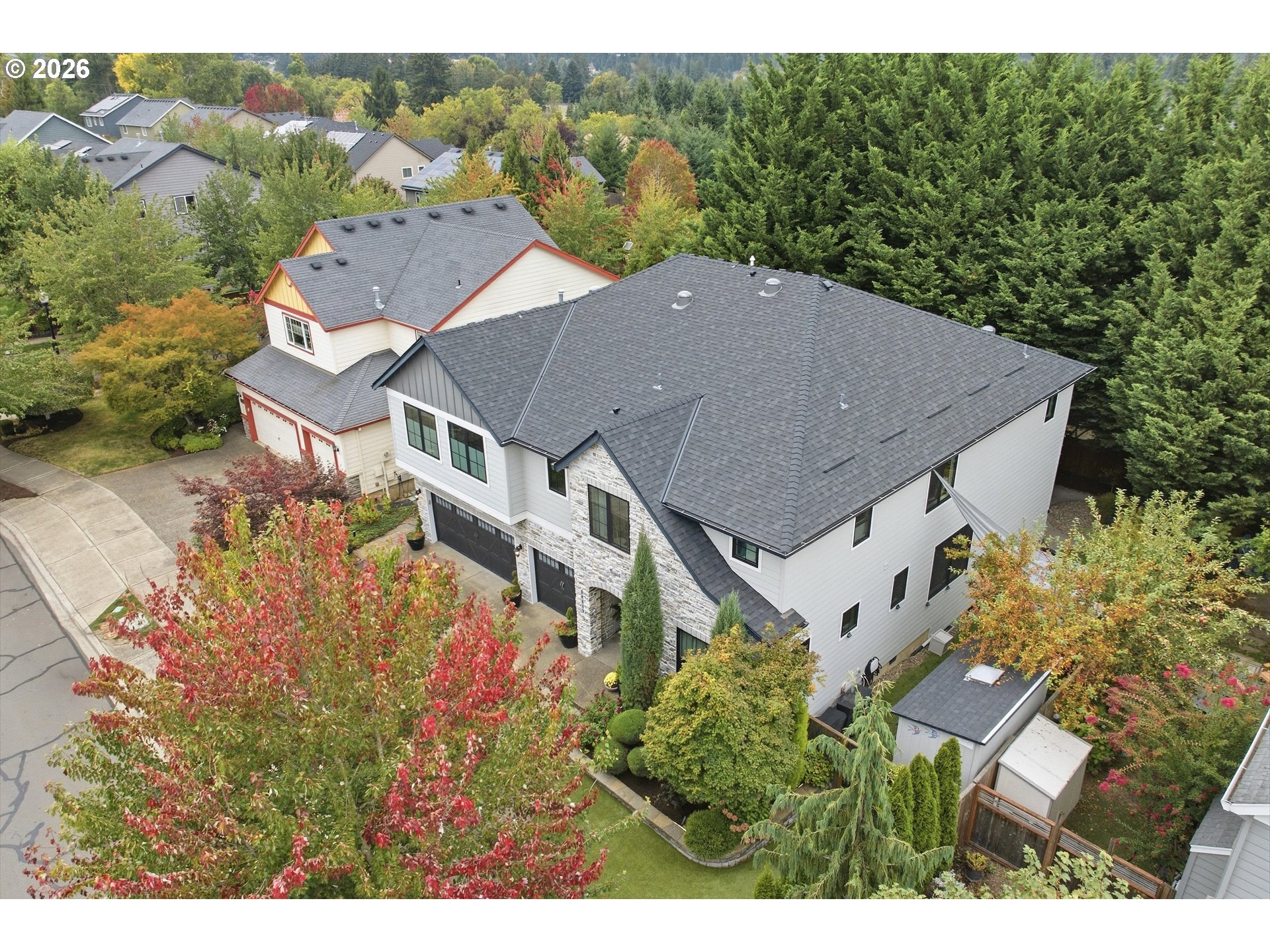 Aerial view of a white multi-level house with a broad gray roof and autumn landscaping.