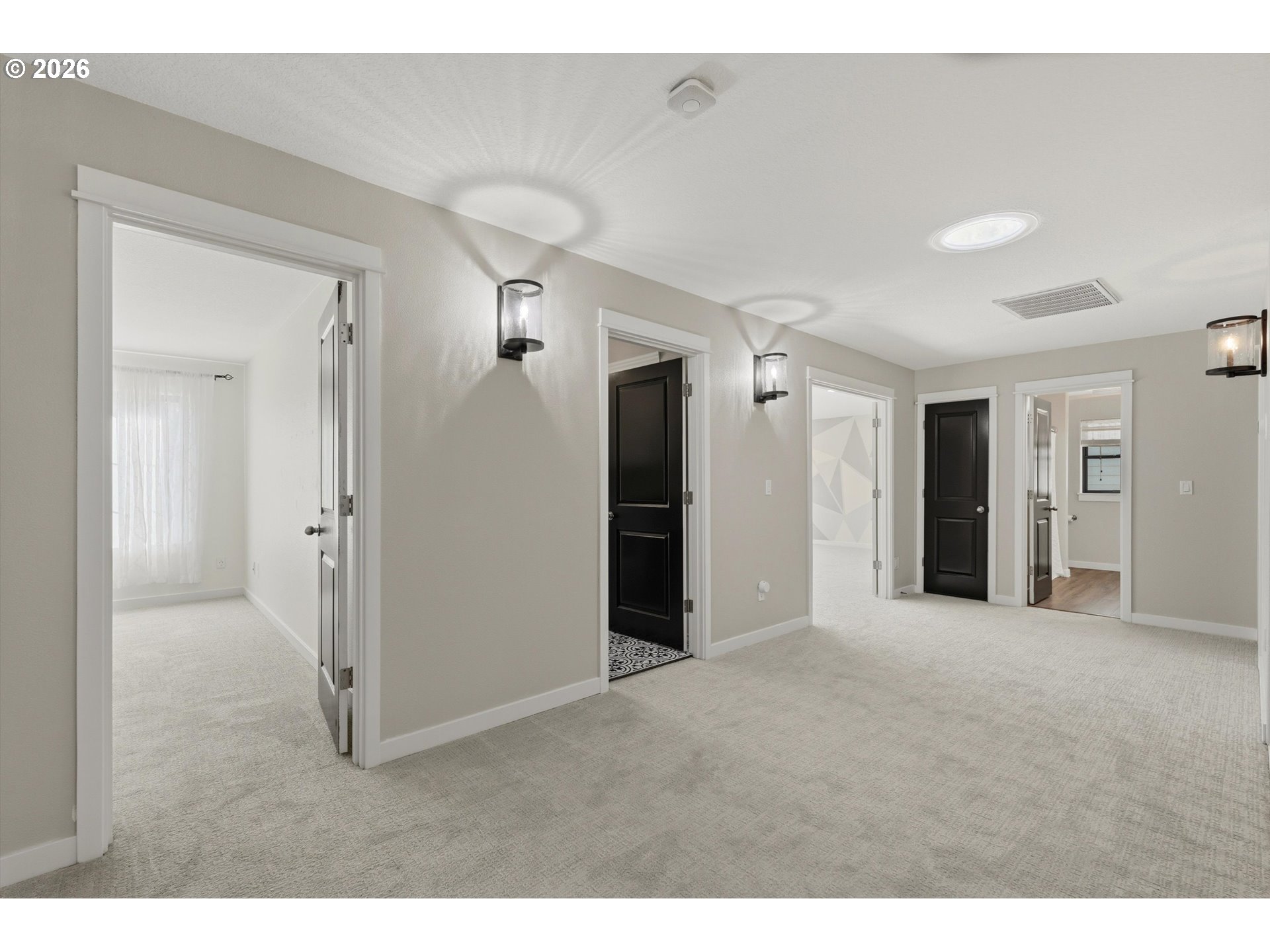 Carpeted hallway with several doorways, black doors, and wall sconces.