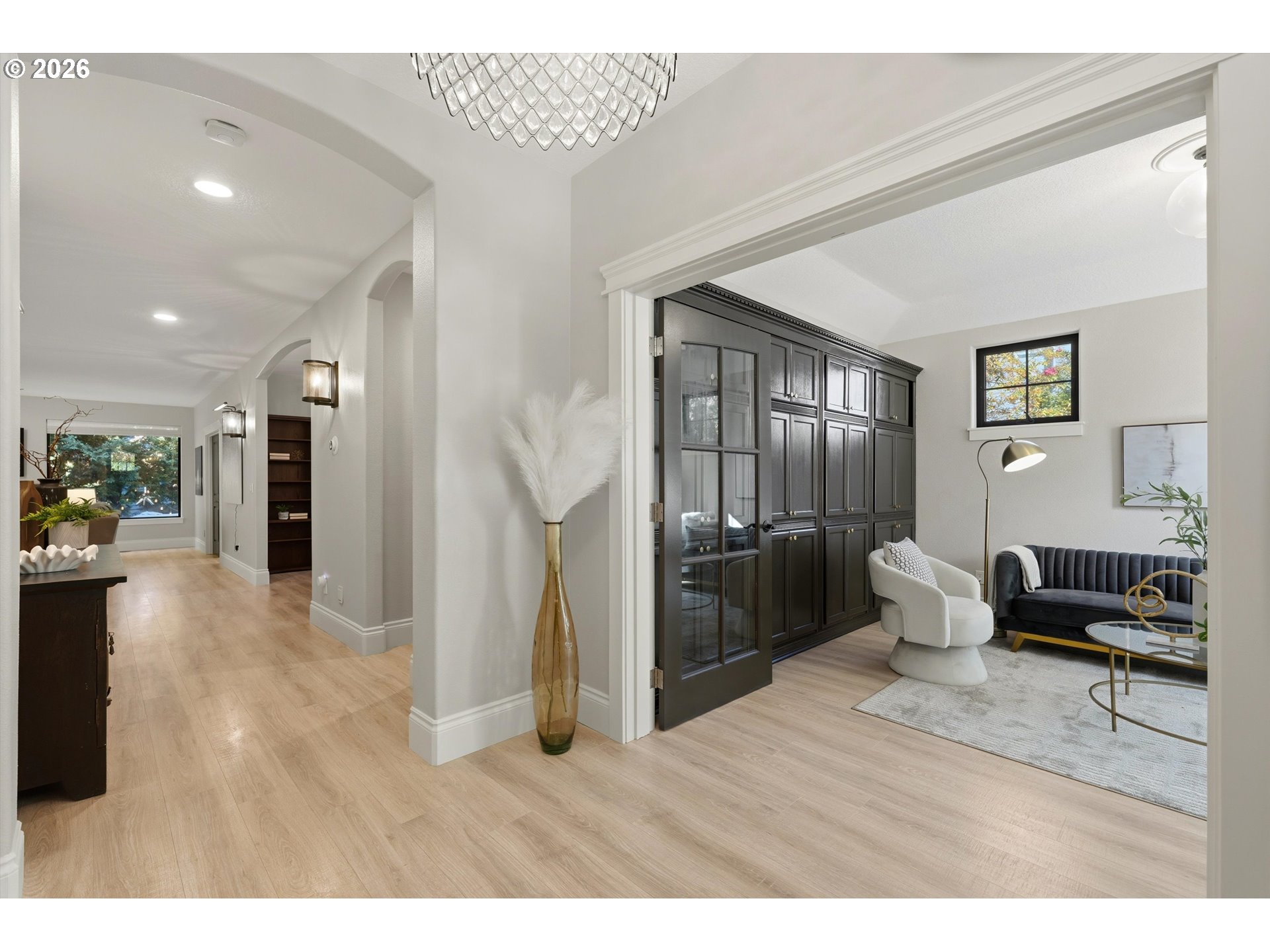 Sitting room with dark built-in cabinetry, navy sofa, and white accent chair beside a bright hallway.