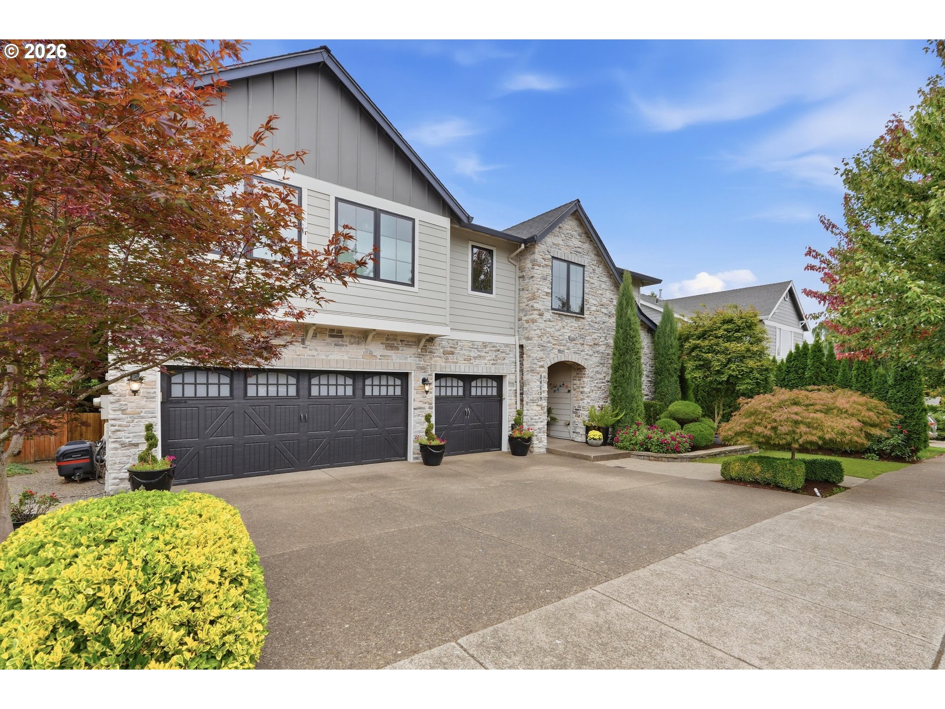 Two-story stone-and-siding home with dark garage doors and landscaped front yard.