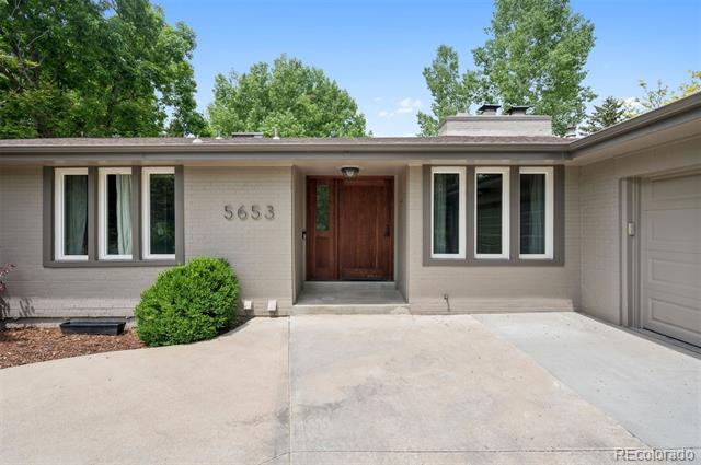 Single-story home with a recessed wooden front door, wide driveway, and address number 5653.