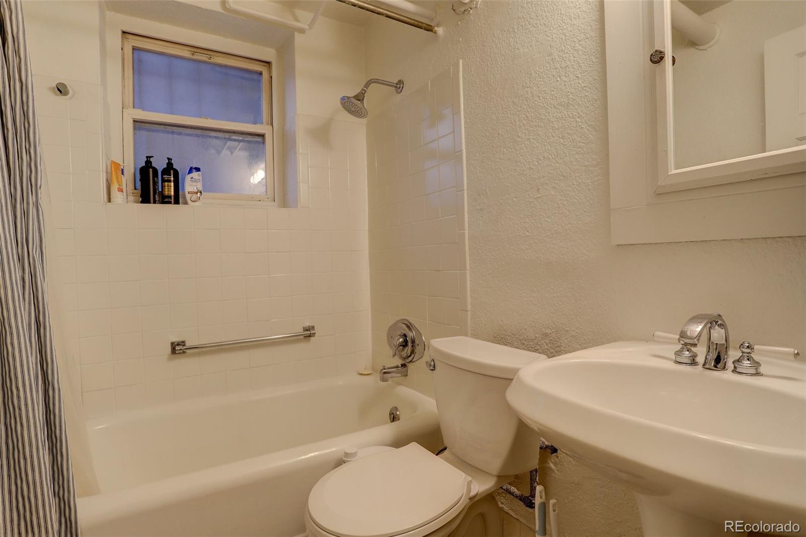 Bathroom with a white bathtub and shower, window, toilet, and sink vanity.