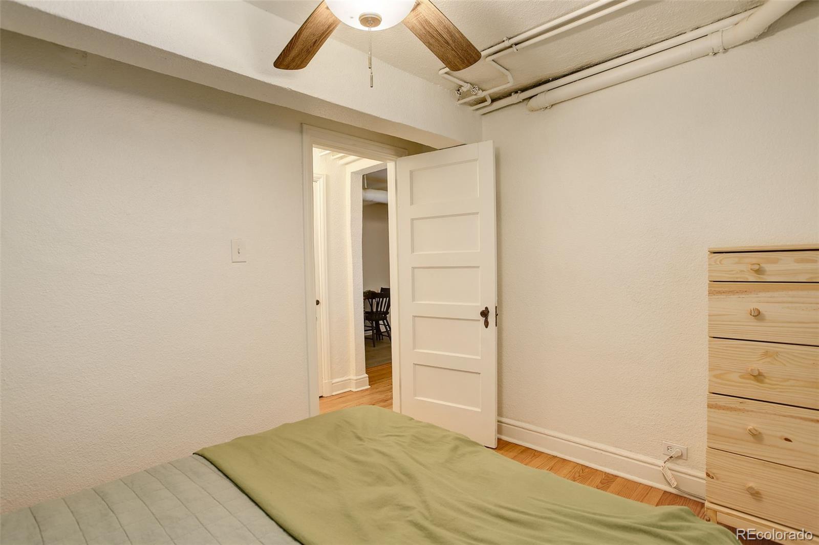 Bedroom with muted green bedding, a ceiling fan, and an open door to the adjoining room.