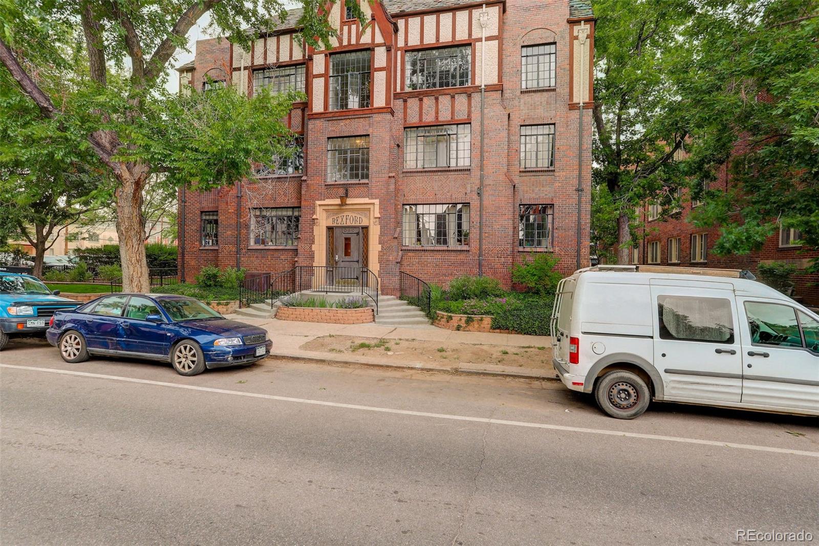 Red-brick apartment building with Tudor-style framing and a Rexford entrance, viewed from the street.