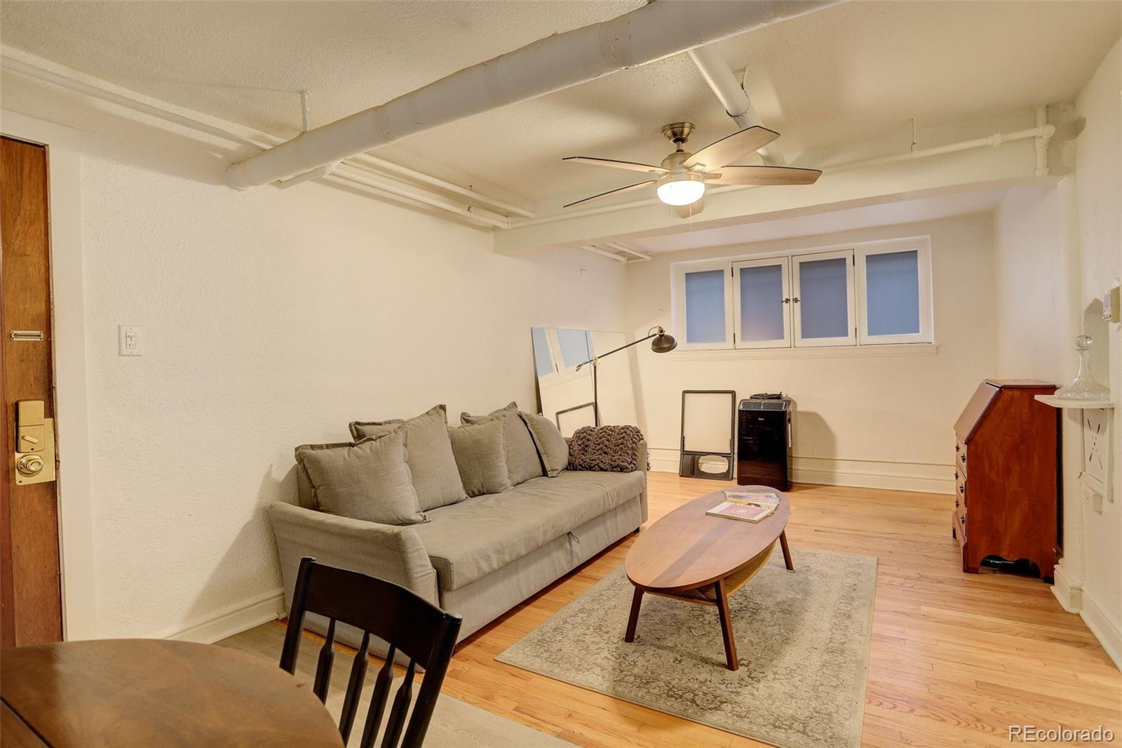 Furnished living room with a gray sofa, oval coffee table, hardwood floors, and exposed ceiling ductwork.