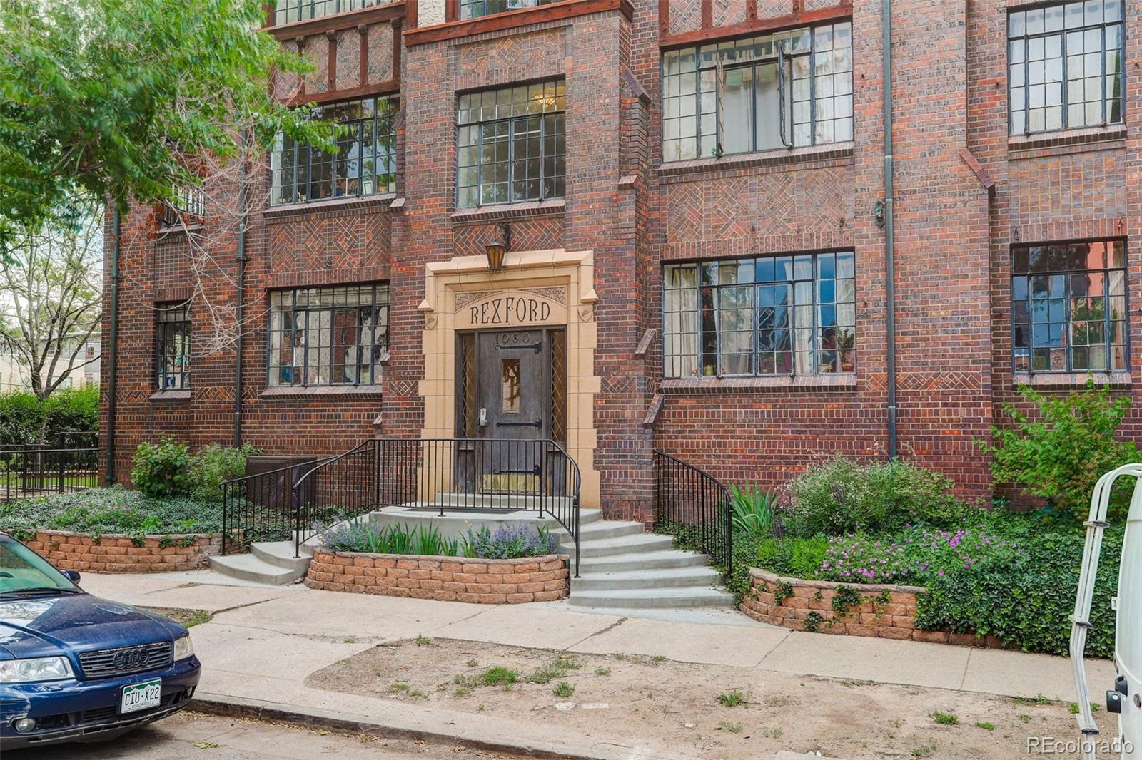 Brick apartment building entrance with a Rexford sign and landscaped steps.