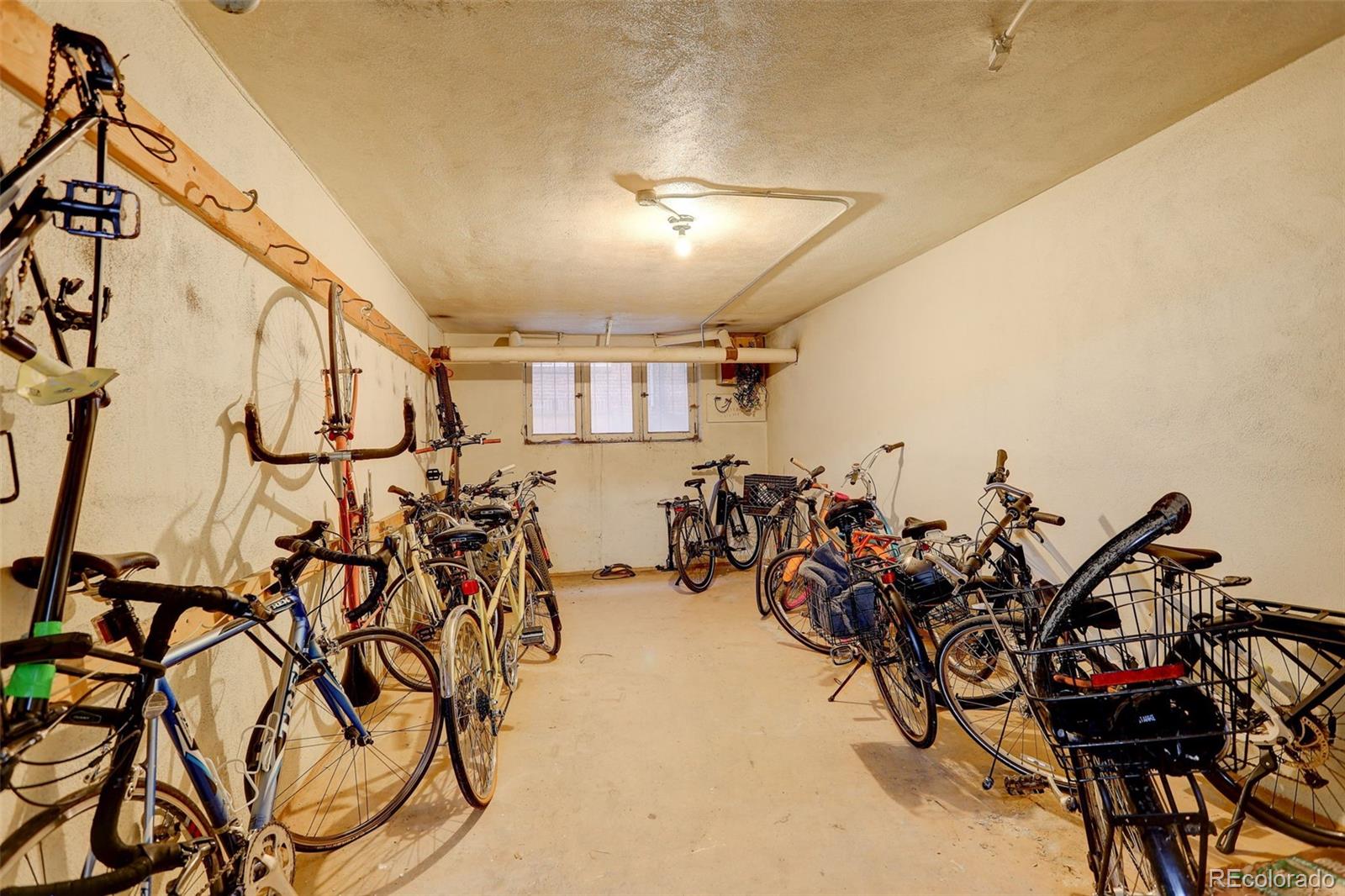 Bicycle storage room with bikes lining both walls and a small window at the far end.