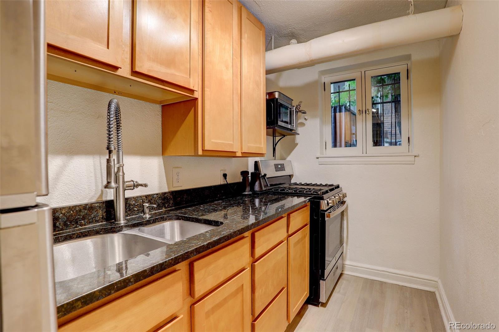Kitchen with honey-colored cabinets, dark granite counters, a spring-coil faucet, and a gas range.