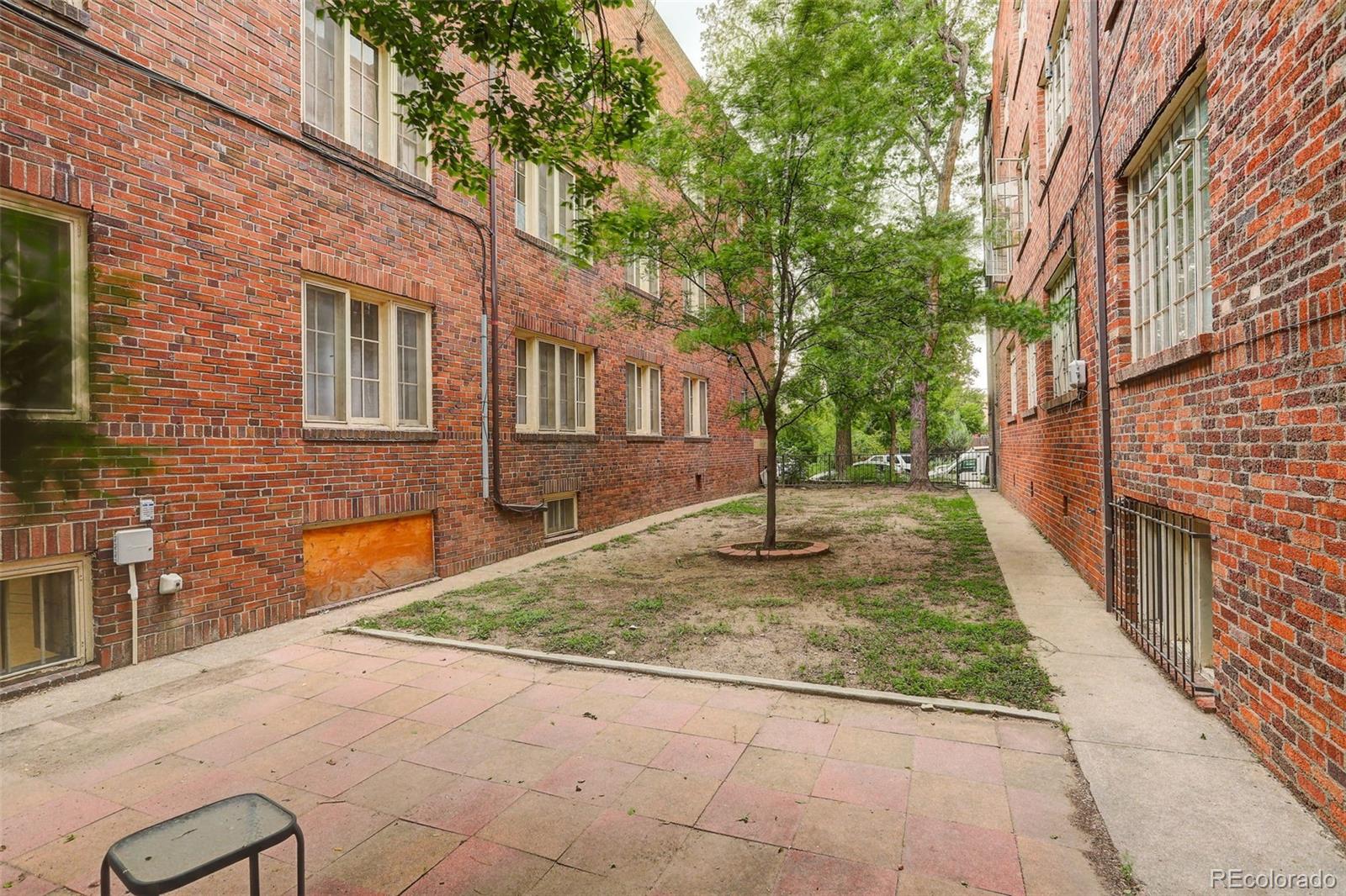Apartment courtyard between red brick buildings, with mature trees and paved walkways.