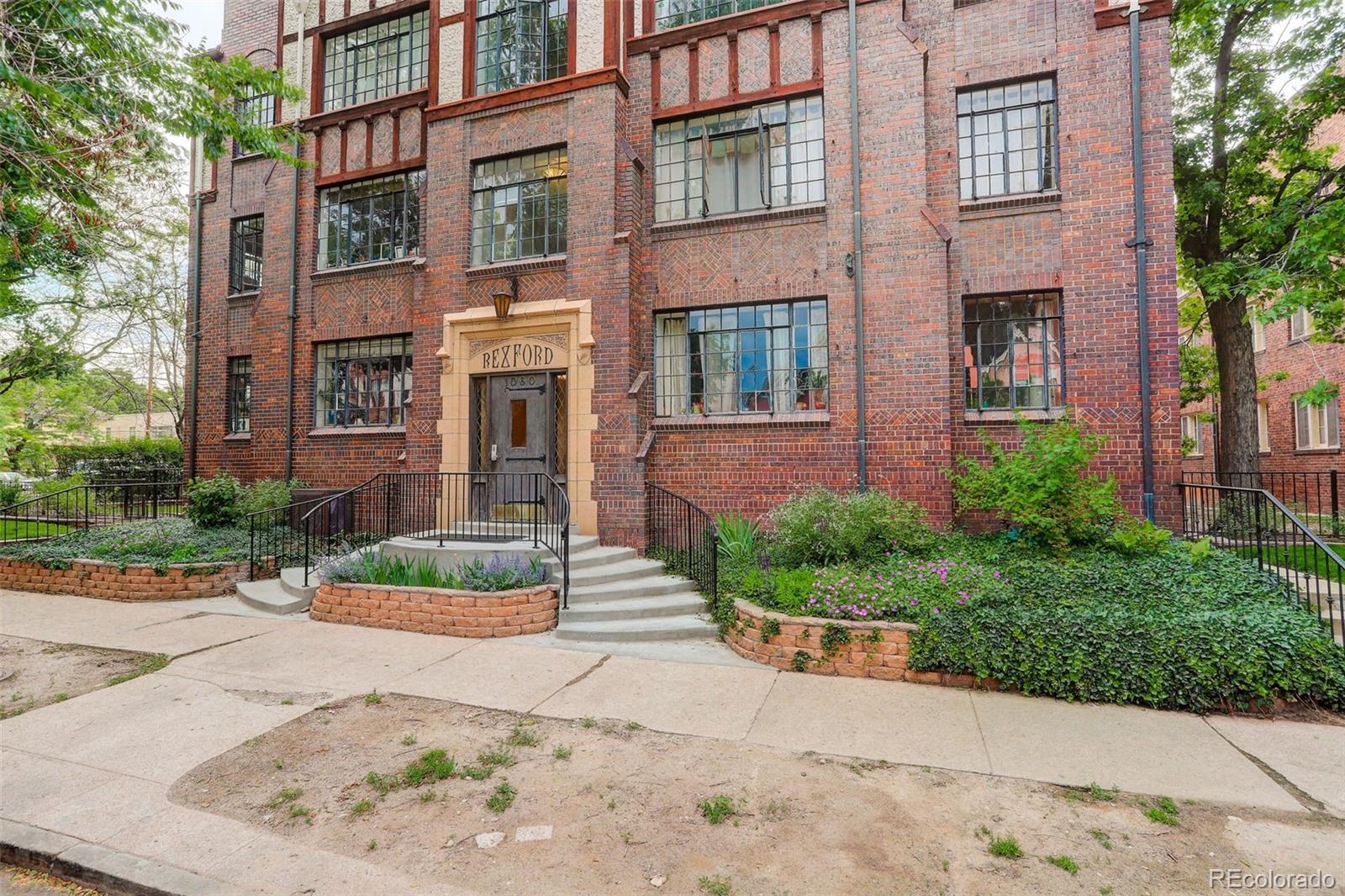 Rexford apartment building with a red brick façade and landscaped front entrance.