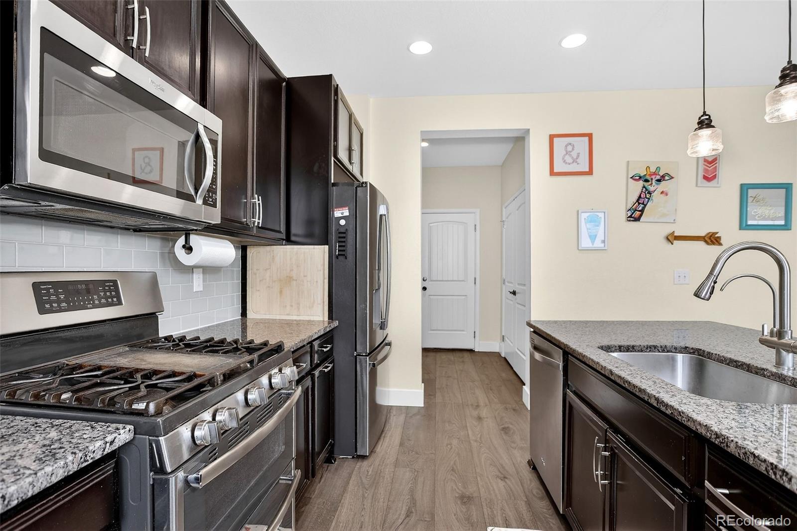 Kitchen with dark cabinets, granite counters, stainless appliances, a gas range, and colorful wall art.