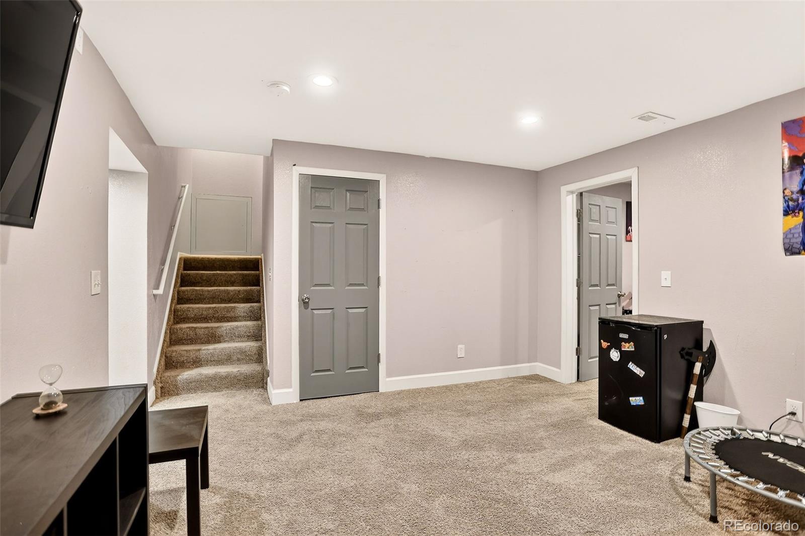 Carpeted room with stairs, two gray doors, a desk, and a mini fridge.