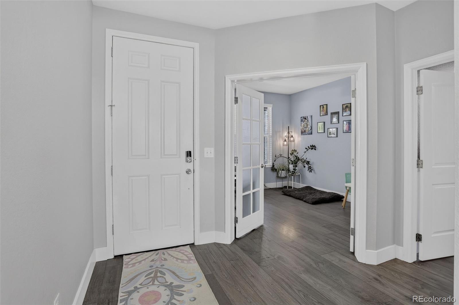 Entryway with a white front door, gray plank flooring, and an open doorway to a furnished sitting area.