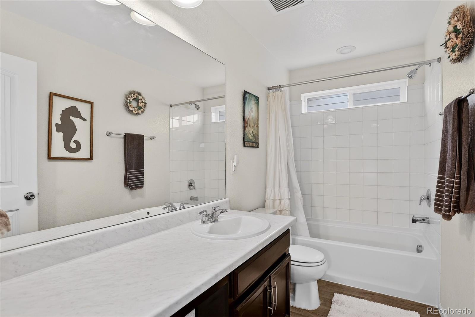 Bathroom with a long vanity, dark wood cabinets, and a white tiled tub surround.